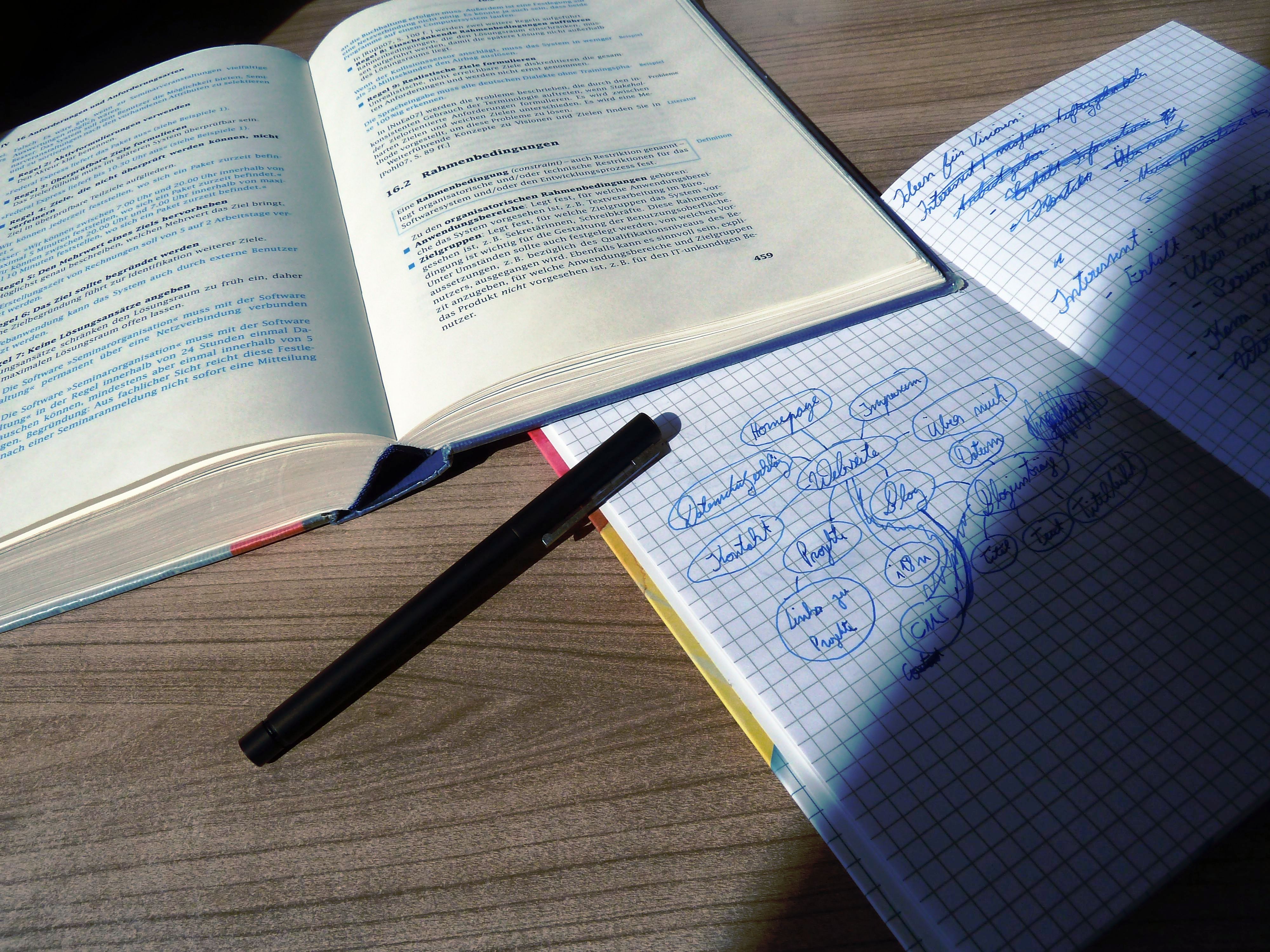 Lehrbuch, Notizbuch und Füllfederhalter auf einem Schreibtisch